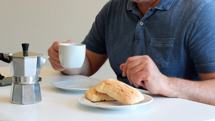 close-up of a man having breakfast at home with biscuits and coffee on white table and natural light coming through the window