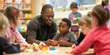 © Iryna - An African kindergarten teacher smiles while children play and learn in a colorful classroom.