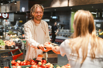 Smiling man giving apple to woman in grocery store