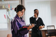 © qunica.com - Focused Indian woman in purple uniform using headset to coordinate tasks in a busy office environment, with colleague in background.