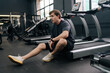 © dikushin - Portrait of tired runner taking break at sport gym sit on treadmill. Portrait of exhausted sweaty male hard breathing after cardio exercise running workout. Weary man sit on fitness treadmill relax.