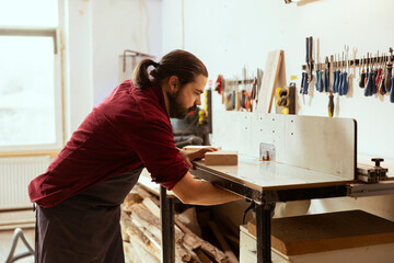 Wall Mural - Man preparing wood shaper machinery, starting work on customer commissioned wooden objects in studio. Woodworker in carpentry shop installing spindle moulder equipment for manufacturing process