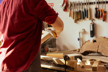 Wall Mural - Woodworker using sandpaper to sander lumber block, making furniture in assembling shop with professional tools in background. Handyman polishing wood with abrasive material during renovation work