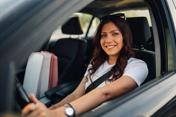 Portrait of shopper girl driving car with shopping bags next to her.