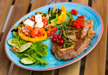 Wall Mural - Fried beef loin decorated with red currant and rosemary with healthy summer salad on wooden background