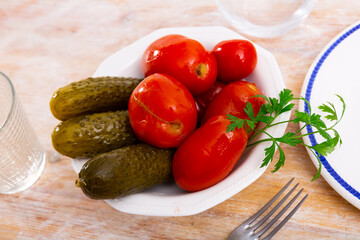 Wall Mural - Appetizing pickled cucumbers and tomatoes on a plate, decorated with a sprig of fresh parsley. Close-up image