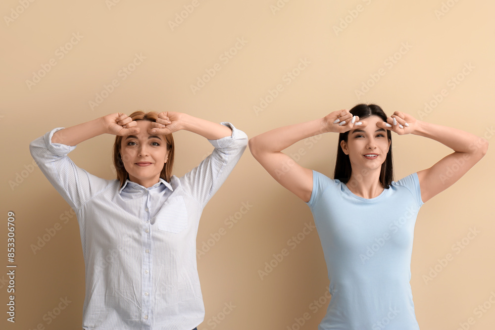 Beautiful happy women doing face building exercise together on beige background