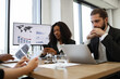 © sofiko14 - Business meeting with diverse professionals analyzing data charts on screen, discussing strategy, using laptop and smartphone. Serious, focused atmosphere with modern office setting.