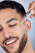© peopleimages.com - Skincare, man and facial oil for beauty with natural glow or shine results in studio. Male person, dermatology and hyaluronic acid serum for acne scar treatment and healthy beard by gray background