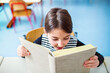© Halfpoint - Portrait of cute schoolgirl sitting at desk reading big book. Student girl in classroom in classroom at the elementary school