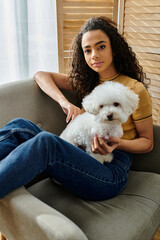 Wall Mural - Woman sits on couch, holding white bichon frise dog.