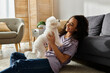 © LIGHTFIELD STUDIOS - A woman seated on the floor tenderly holding a white Bichon Frise dog.