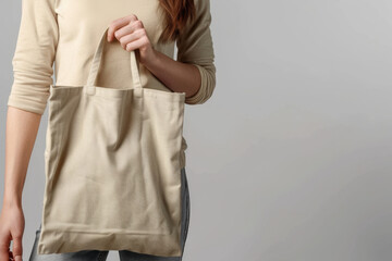 Woman holding an eco-friendly textile bag against a grey background, emphasizing sustainability. Perfect for showcasing designs or messages