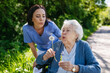 © Halfpoint - Female caregiver and senior woman in wheelchair holding dandelion, picking wild flowers. Nurse and elderly woman enjoying a warm day in nursing home, public park.