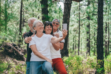 Canvas Print - Group of senior friends enjoying a trekking day in the forest, elderly caucasian couples of retirees smiling carefree take selfie with smartphone, healthy lifestyle in outdoors concept