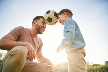 Wall Mural - Soccer ball, holding it by heads, fun. Happy father with son are on the field at summertime