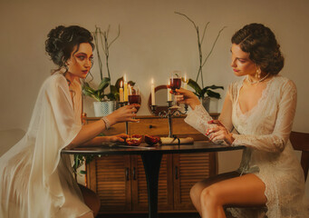 Two women Sexy girl beauty face lips sitting at the dinner table luxury light room. vintage nightie silk white long dress fairy old style noble lady girls holds glass wine drink clink glasses toast