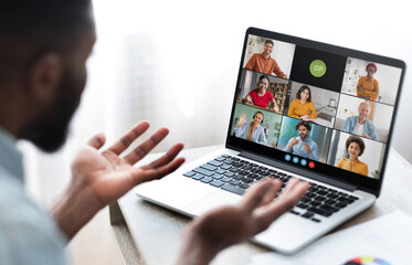 Poster - Black man sits in front of a laptop, participating in a video conference meeting with several colleagues. He has his hands raised as if he is making a point during the call.