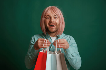 Wall Mural - Holding shopping bags. Gay man with pink hair is standing against green background