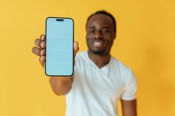 Wall Mural - Blue colored smartphone for copy space in hand. Black man is in the studio against yellow background