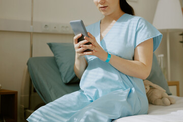 Wall Mural - Young pregnant woman texting via mobile phone while she sitting in ward