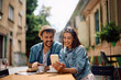 © Drazen - Happy couple having cup of coffee while using mobile phone in sidewalk cafe.