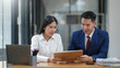 © amnaj - Two business professionals in a modern office discuss documents, exemplifying teamwork and collaboration.