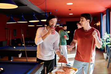 Wall Mural - Friends enjoy a casual game of billiards in a stylishly decorated venue, sharing pizza and drinks.