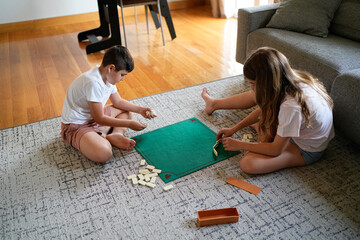 Two children playing with dominoes on a carpeted floor