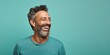 © Hanna Haradzetska - Portrait photo of a happy Middle Eastern man, 46 years old, winking on a pastel teal background