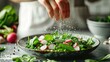 © Pinklife - A chef's hand sprinkling salt on a fresh green salad with radishes, detailed image with a dynamic feel