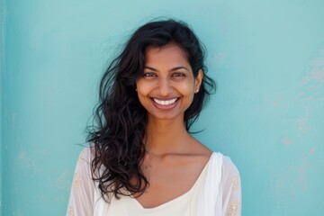 Wall Mural - Portrait of a happy indian woman in her 20s smiling at the camera isolated in pastel blue background