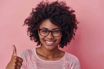 Wall Mural - Portrait of a joyful afro-american woman in her 30s showing a thumb up in front of pastel pink background