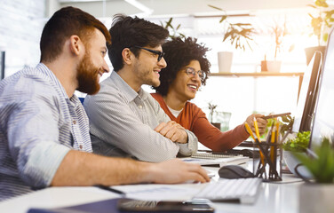 Poster - A diverse group of coworkers are gathered around a computer, engaging in a collaborative discussion or working on a project together. They appear focused and attentive to the screen