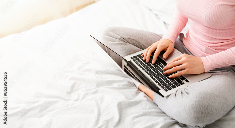 Woman is sitting on a bed, absorbed in her laptop computer. She appears ...