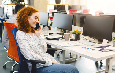 Aufkleber - A woman sitting at a desk, engaged in conversation on her cell phone. She appears focused and attentive while speaking. The desk is neat and organized, with a computer and stationery on it.