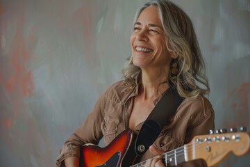 Wall Mural - Portrait of a grinning woman in her 40s playing the guitar isolated in pastel gray background