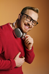 Wall Mural - Stylish man in red sweater energetically holds headphones.