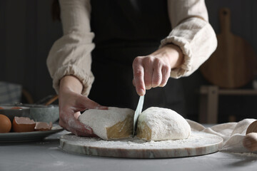 Wall Mural - Woman cutting dough at grey table, closeup