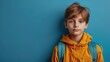 © evgenia_lo - Serious Caucasian boy with a backpack and hoodie against a blue background. Back to school background with caucasian young schoolboy and copy space