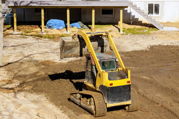 An earthmoving tractor is leveling ground at construction site for cleaning backyard