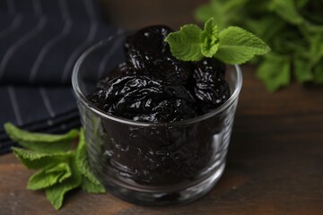 Wall Mural - Tasty dried plums (prunes) in glass bowl and mint leaves on wooden table, closeup