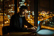 © Arman Zhenikeyev - AI Image. Mature businessman using laptop while sitting in coworking space at night