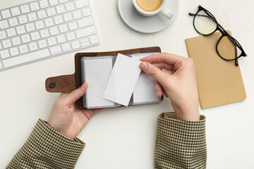 Wall Mural - Woman holding leather business card holder with blank cards at white table, top view