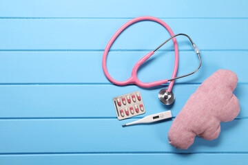 Canvas Print - Pillow, stethoscope, thermometer and pills on light blue wooden background, flat lay. Space for text