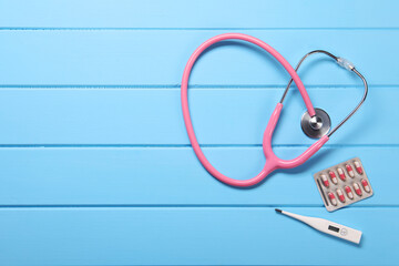 Canvas Print - Stethoscope, thermometer and pills on light blue wooden background, flat lay. Space for text