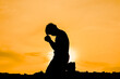 © STOCK PHOTO 4 U - Silhouette of a Person Praying at Sunset with a Vibrant Orange Sky in the Background