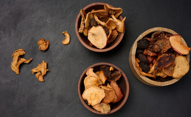 Wall Mural - Dried apple pieces in a wooden round plate on a black table, top view