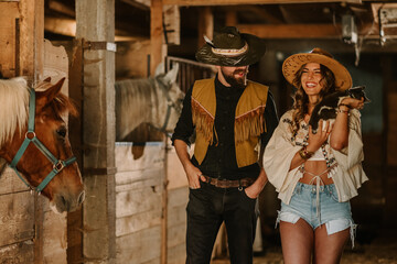 Wall Mural - Young farmer couple with cat in hands walking at horse stable.