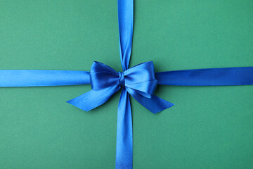 Wall Mural - Blue satin ribbon with bow on green background, top view
